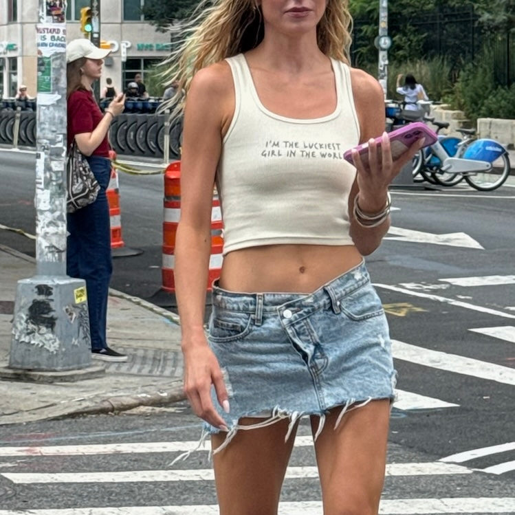 Woman in a crop top and denim skirt standing on a city street.